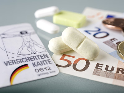 Eine Versichertenkarte, verschiedene Tabletten und Euro-Geldscheine und Münzen.